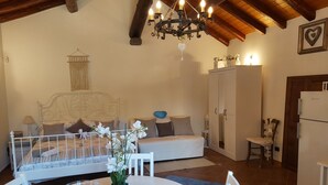 A cozy room with a bed, a white sofa, a dining table with chairs, a chandelier, and a wardrobe.