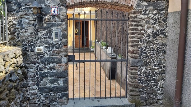 A stone gate with a metal fence, a small window with a number plate, and a door leading to a tiled entrance.