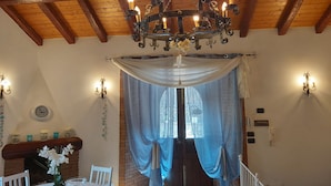 A room with a wooden ceiling, a chandelier, a dining table with chairs, a fireplace, and a window with curtains.