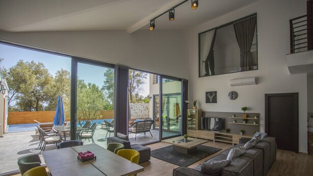 Ein geräumiger Wohnbereich mit einer großen Schiebeglastür, die auf eine Terrasse im Freien führt, einer Couch, einem Couchtisch und einer TV-Konsole.