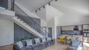 Eine moderne Wohnung mit grauem Sofa, einer Treppe, einem Essbereich und einer Küche.