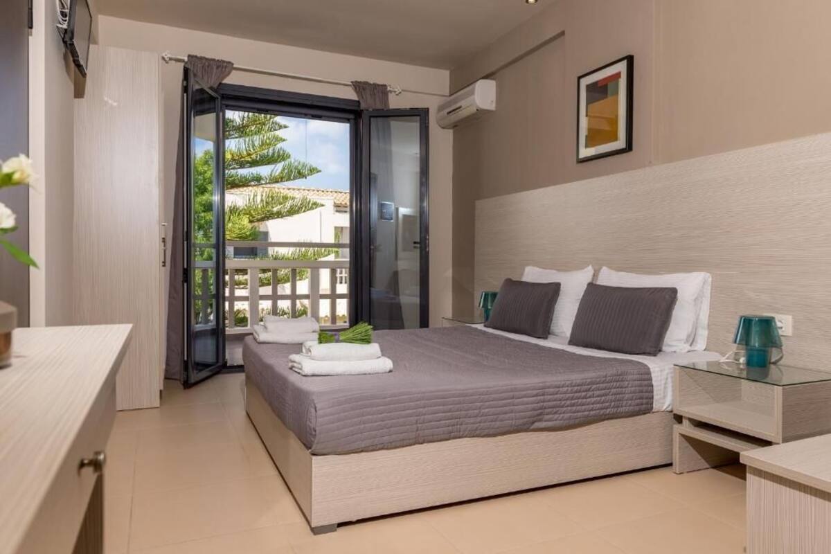 A modern bedroom with a large bed, a glass door leading to a balcony, and a small bedside table.