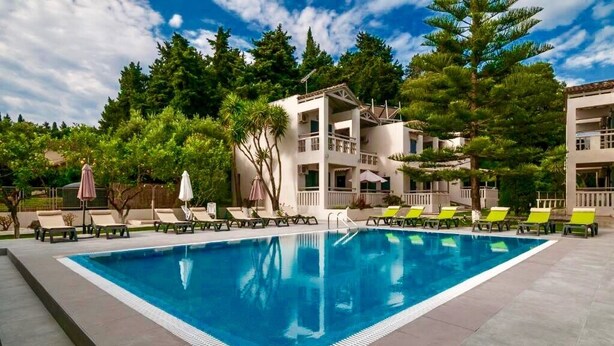 Una piscina con sillas de descanso, rodeada de árboles y un edificio con balcones.