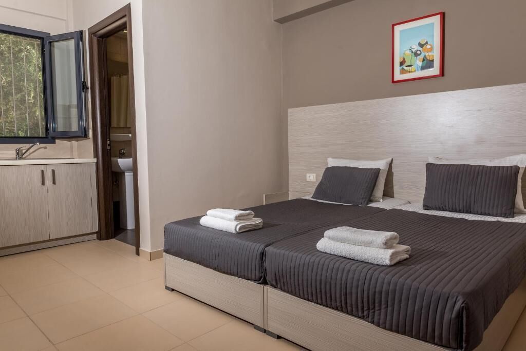 A hotel room with a bed, a nightstand, a window, a bathroom, and a painting on the wall.