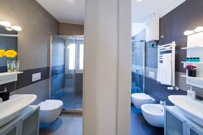 Un baño moderno con cabina de ducha de vidrio, dos inodoros y un bidé.