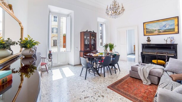 A spacious living room with a dining area, a piano, and a large chandelier.