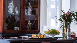 A dining table with a fruit bowl, teacups, and a decorative cabinet in the background.