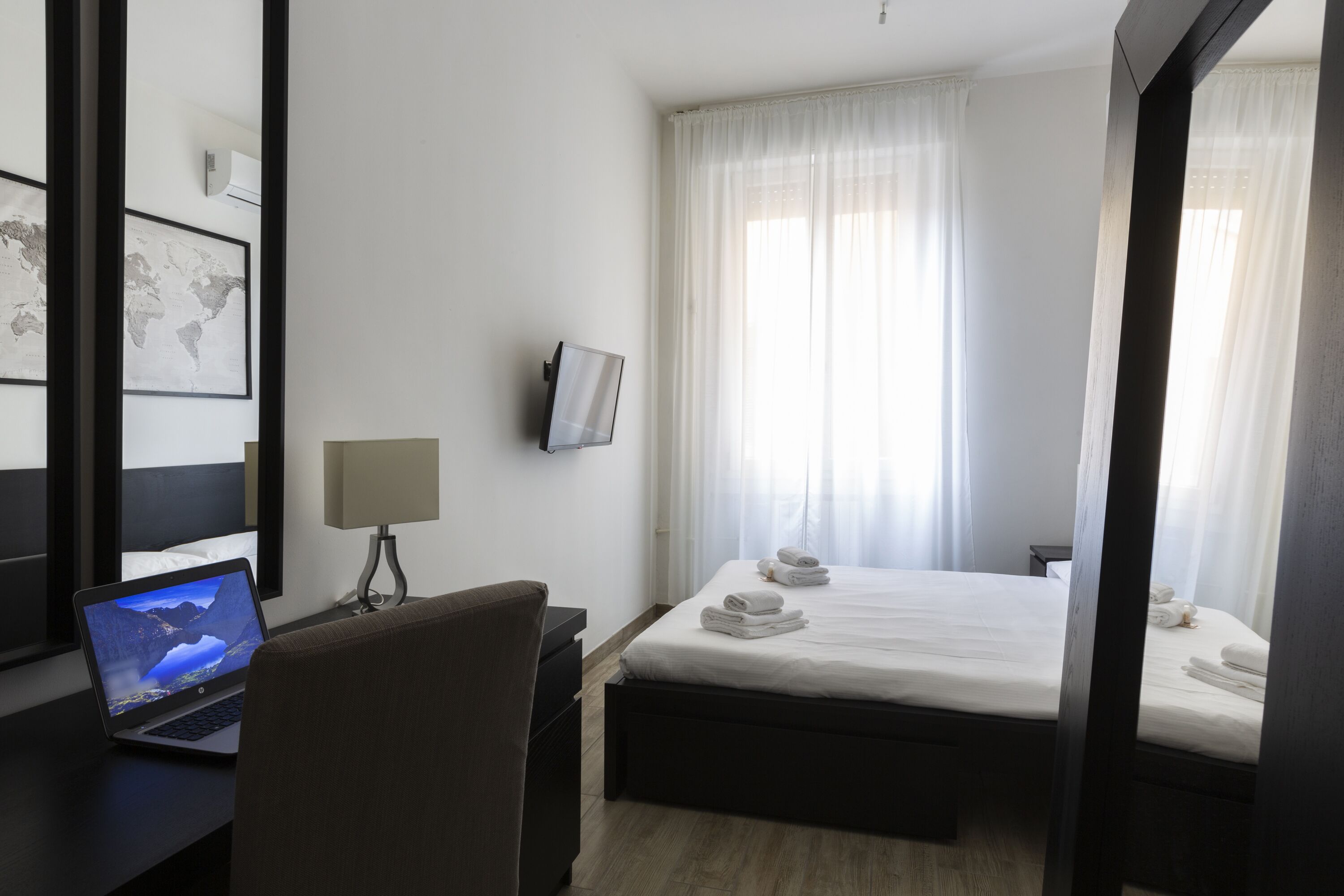 Une chambre d’hôtel avec un lit, un bureau avec un ordinateur portable, une chaise, une table de chevet, une lampe et une carte du monde accrochée au mur.