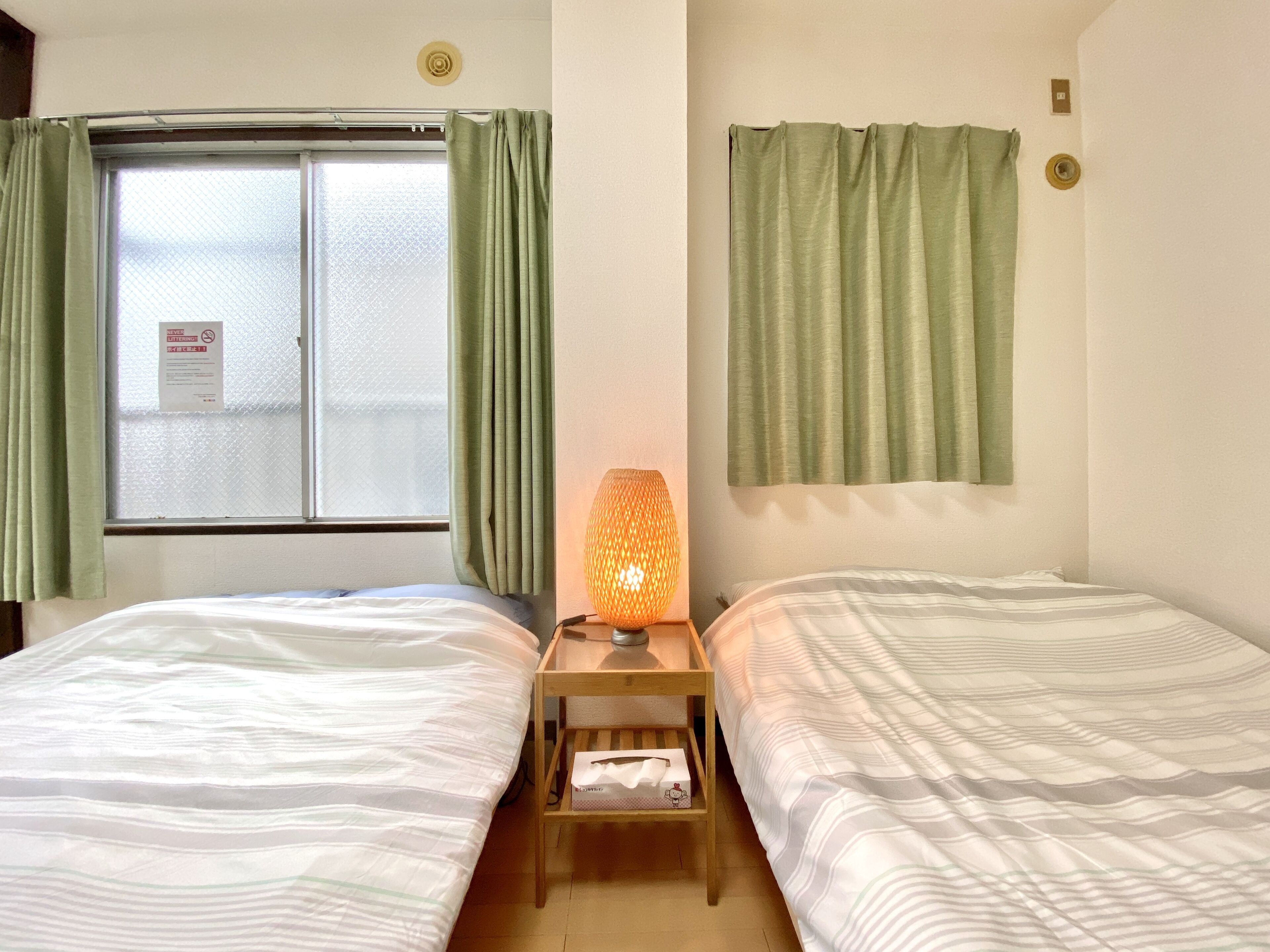 A hotel room with two beds, a window with frosted glass, and a lamp on a bedside table.