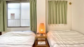 A hotel room with two beds, a window with frosted glass, and a lamp on a bedside table.