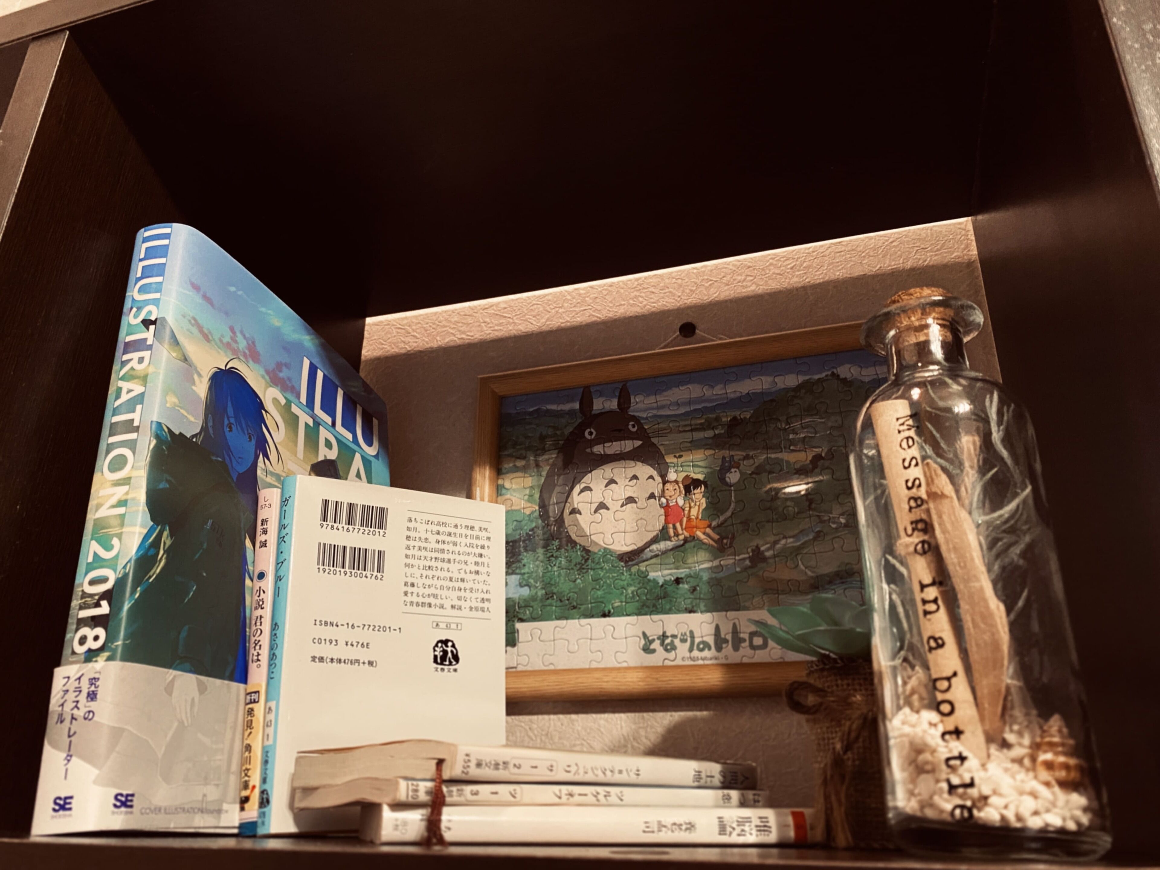 A shelf with books, a puzzle, and a glass bottle.