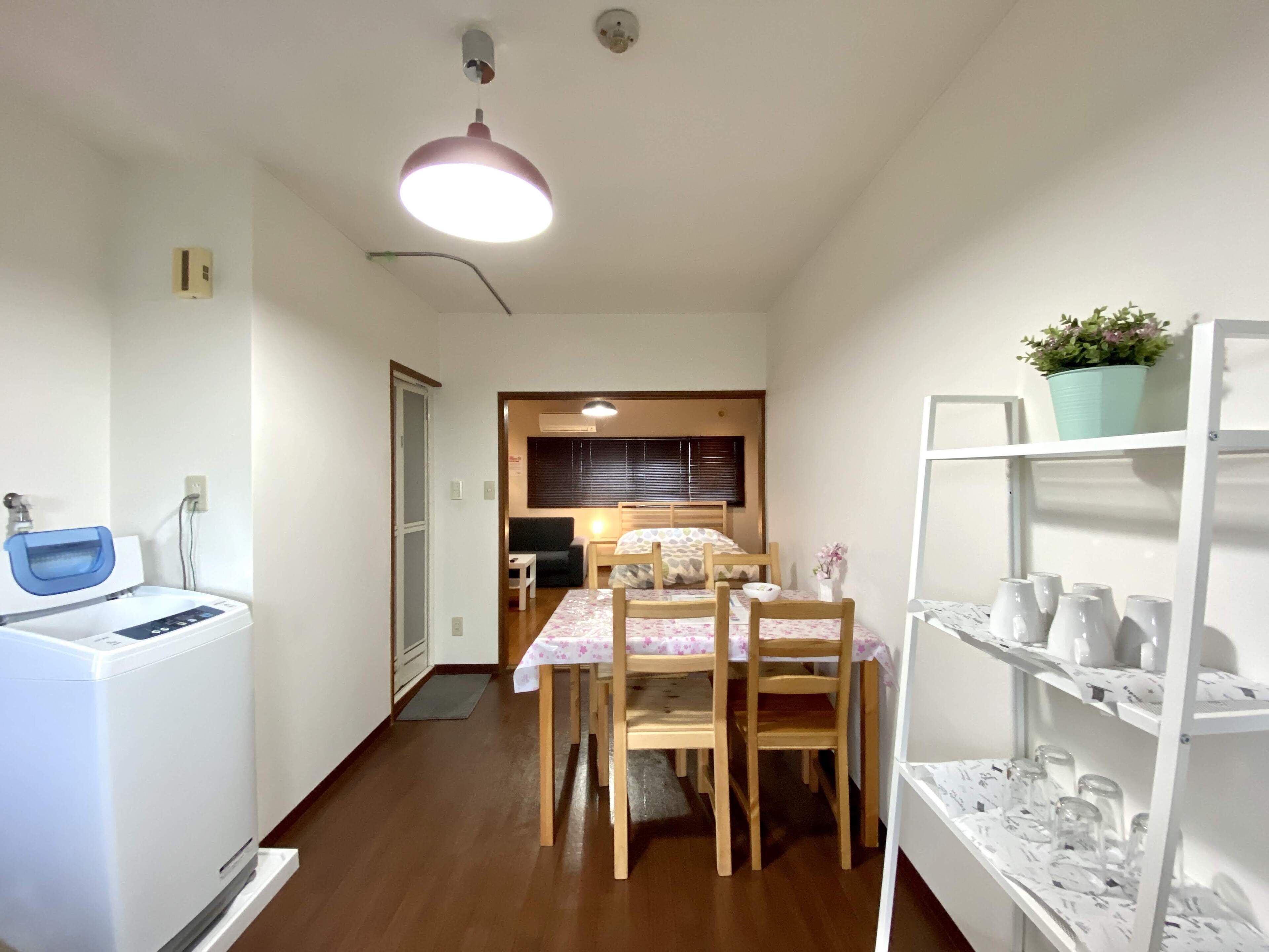 Une cuisine compacte équipée d’un lave-linge, d’un coin repas avec une table et des chaises, et d’une étagère pour ranger la vaisselle.