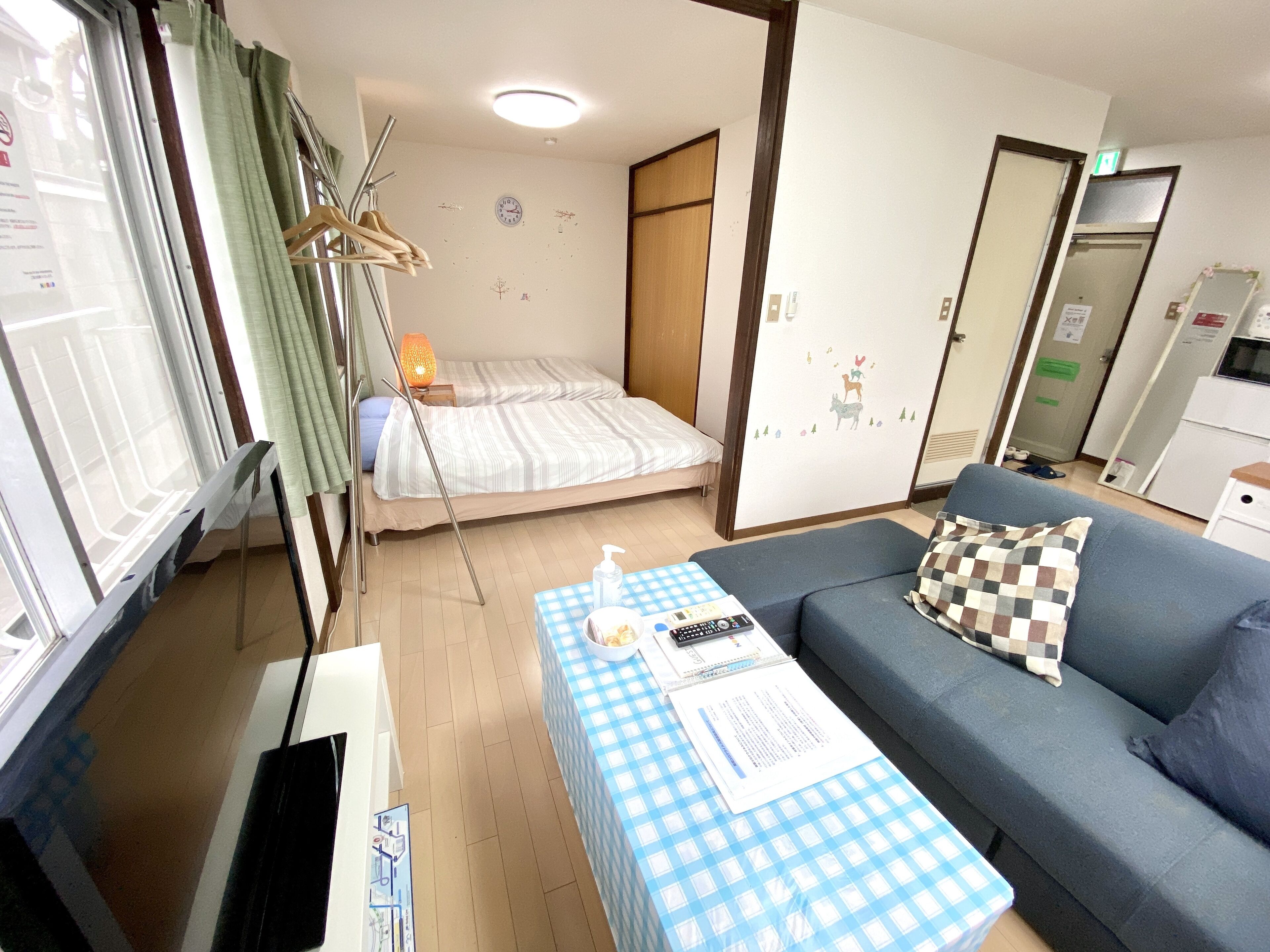 A small, well-lit room with a bed, a sofa, a table with a checkered tablecloth, and a lamp.