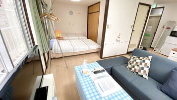 A small, well-lit room with a bed, a sofa, a table with a checkered tablecloth, and a lamp.