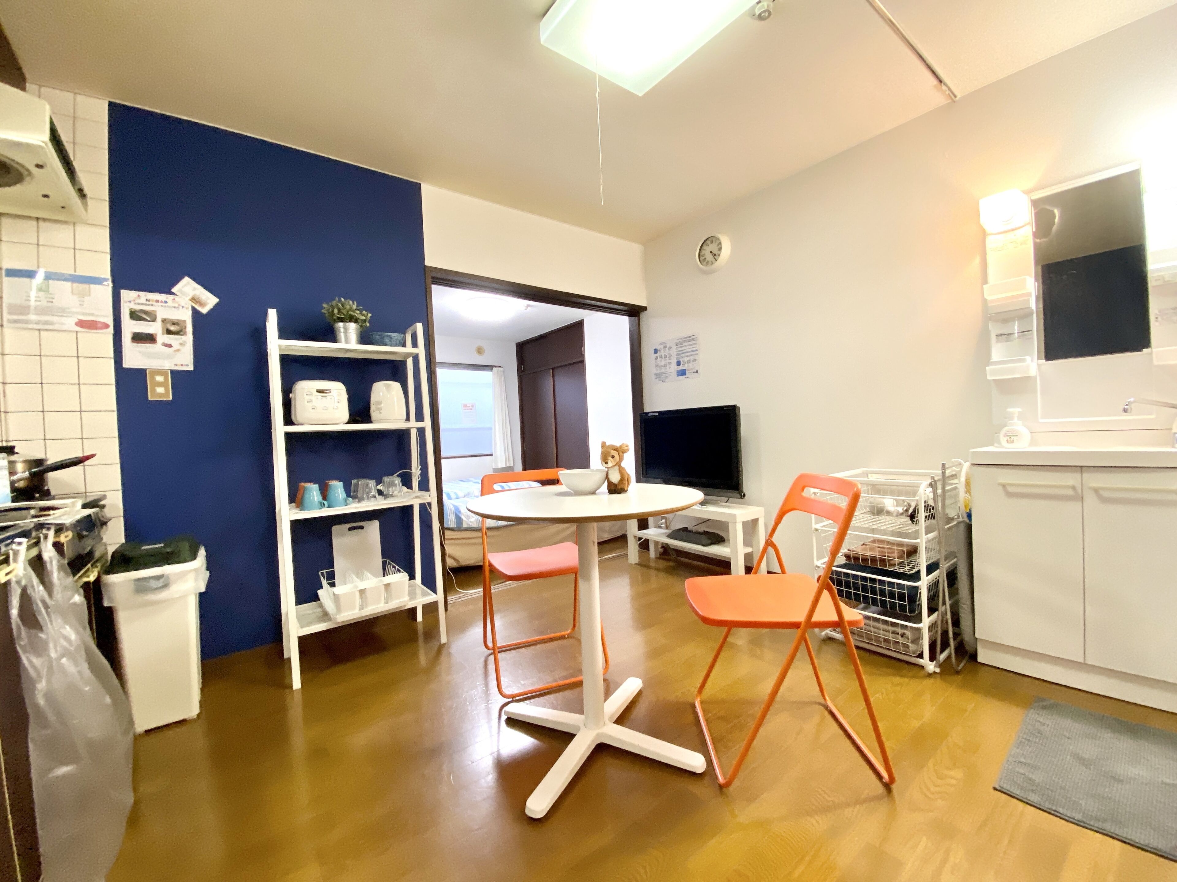 Una cocina compacta con electrodomésticos blancos, una pared de acento azul y una zona de comedor con sillas naranjas.