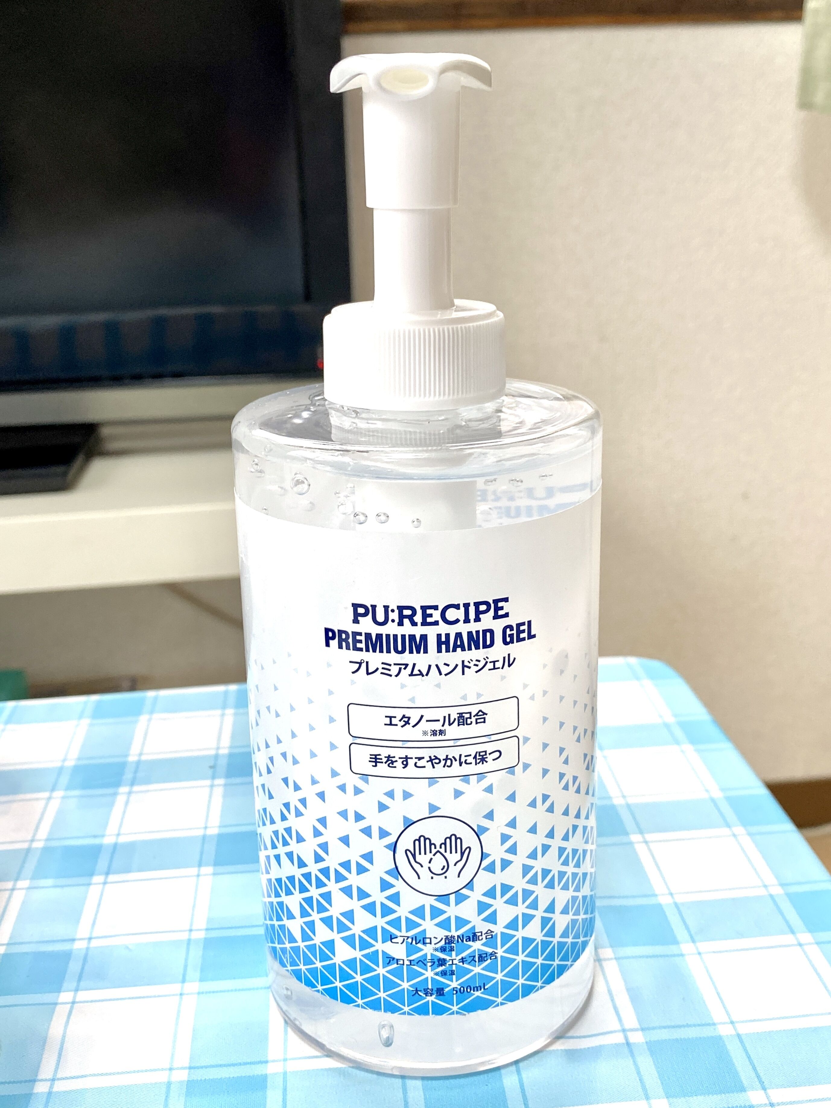 A bottle of PURERECIPE PREMIUM HAND GEL on a blue and white checkered tablecloth.