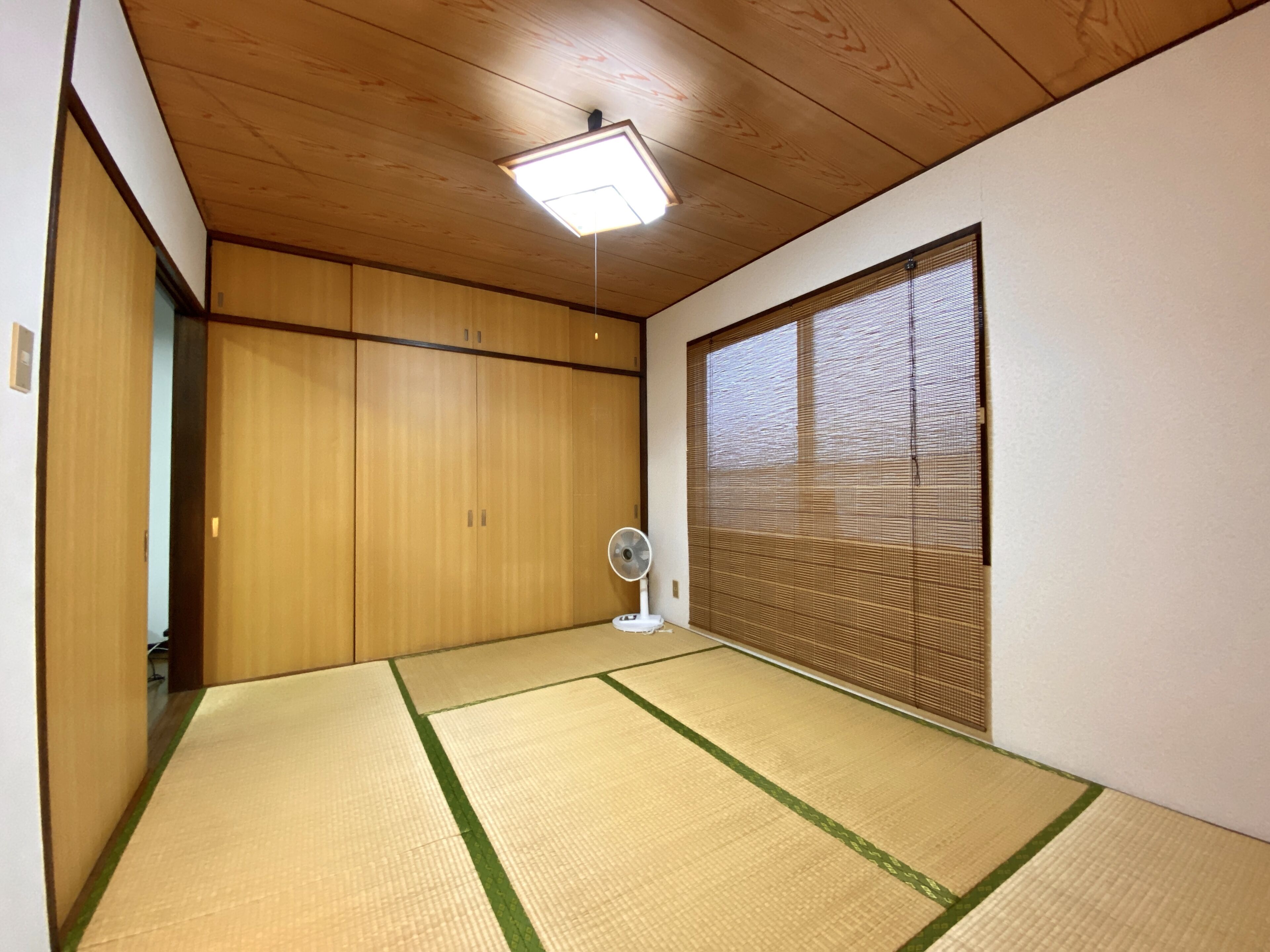 Ein Zimmer mit Tatami-Matten, einer Schiebetür, einem Deckenventilator und einem Fenster mit Jalousien.