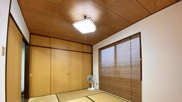 Ein Zimmer mit Tatami-Matten, einer Schiebetür, einem Deckenventilator und einem Fenster mit Jalousien.