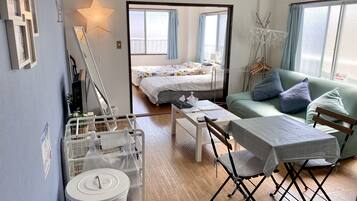 A compact hotel room with a bed, a sofa, a dining table, and a small kitchen area.