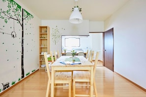 A dining area with a wooden table, chairs, and a hanging light fixture. - NOMAD Take Five (Matsudo)