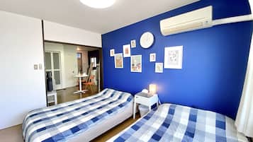 A bedroom with two beds, a desk, and an air conditioning unit on the wall.