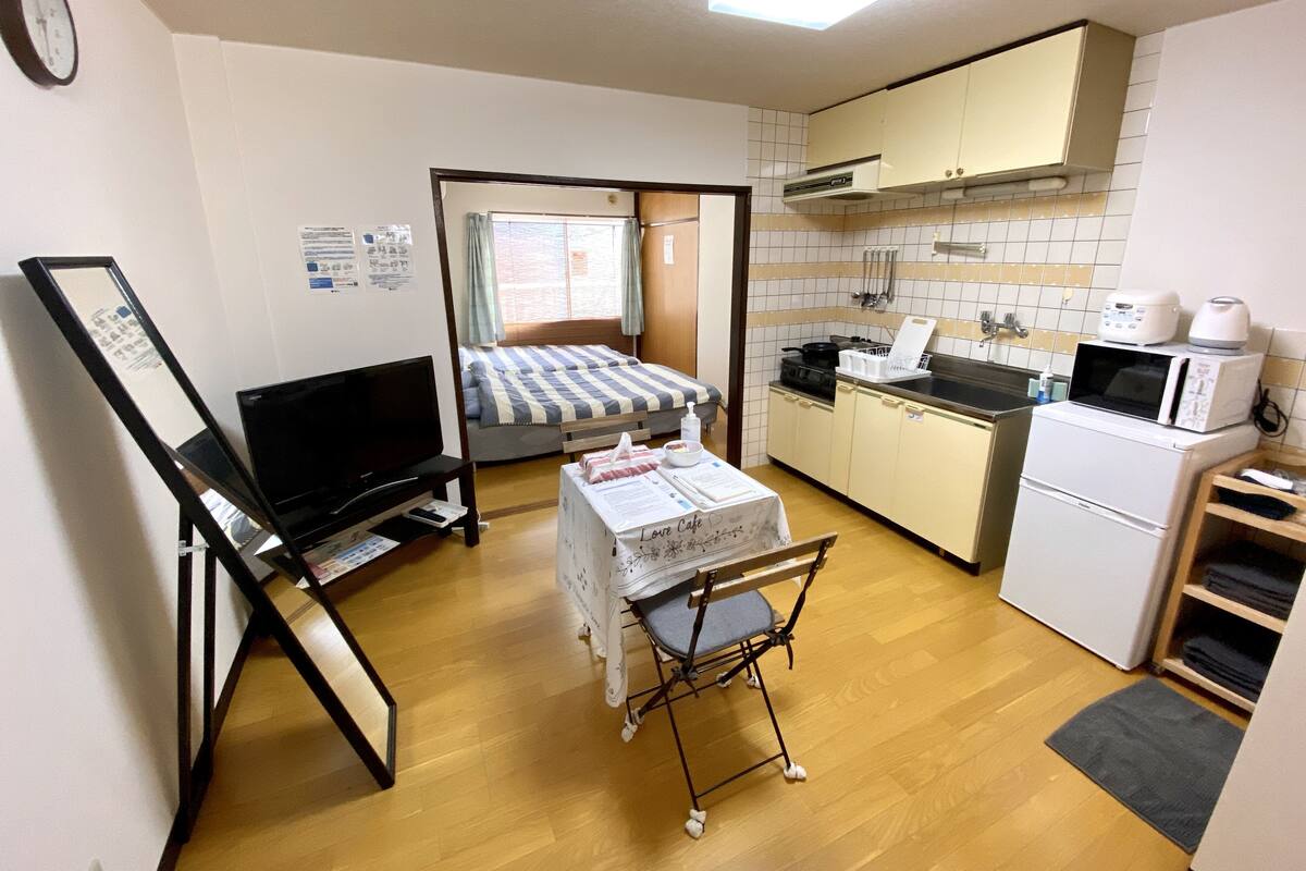 Habitación compacta con cama, una mesita, televisor, kitchenette y microondas.