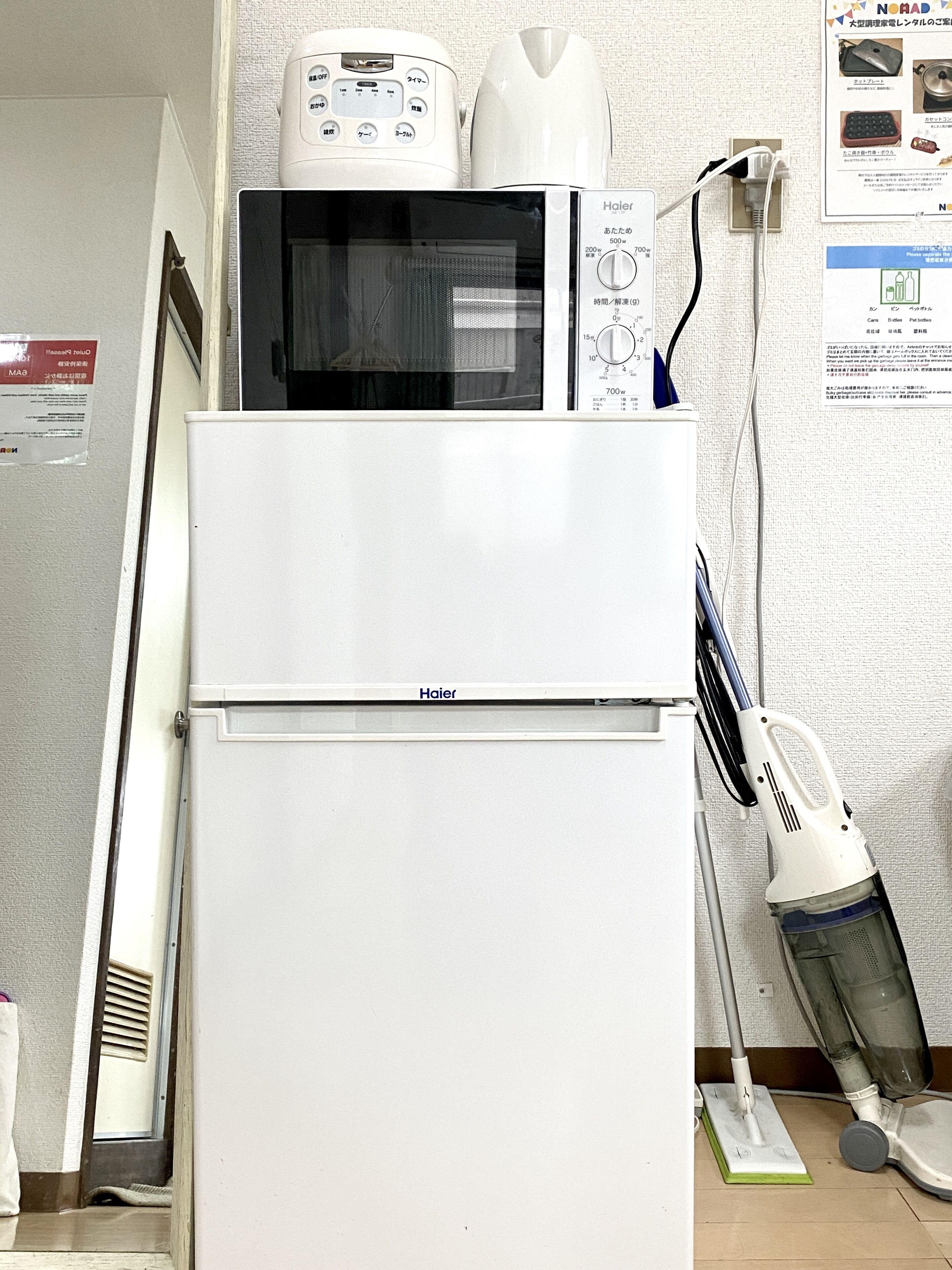 Un refrigerador blanco de Haier con un microondas encima, una aspiradora y una regleta de enchufes en la pared.