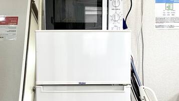 Un refrigerador blanco de Haier con un microondas encima, una aspiradora y una regleta de enchufes en la pared.