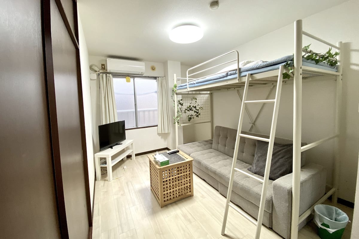 Una habitación pequeña con literas, un sofá, un televisor y una mesita.