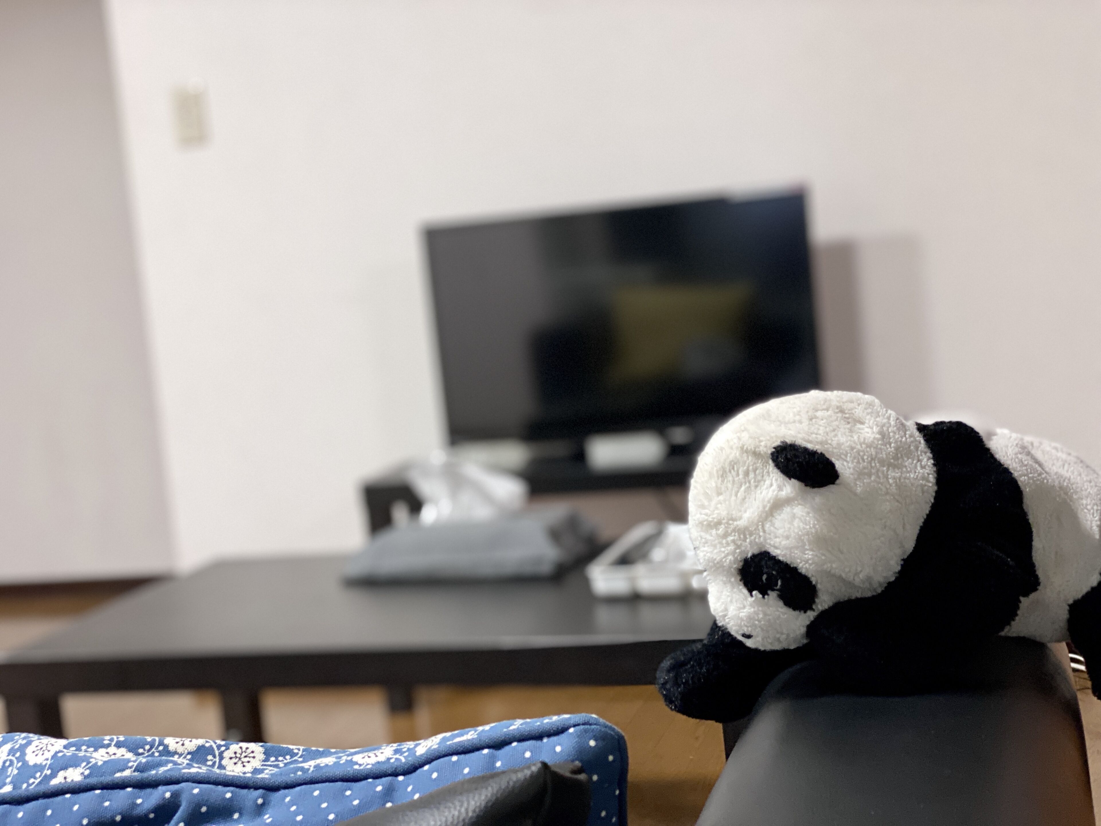 A plush panda toy on a chair in a room with a television and a desk in the background.