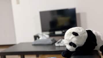 A plush panda toy on a chair in a room with a television and a desk in the background.