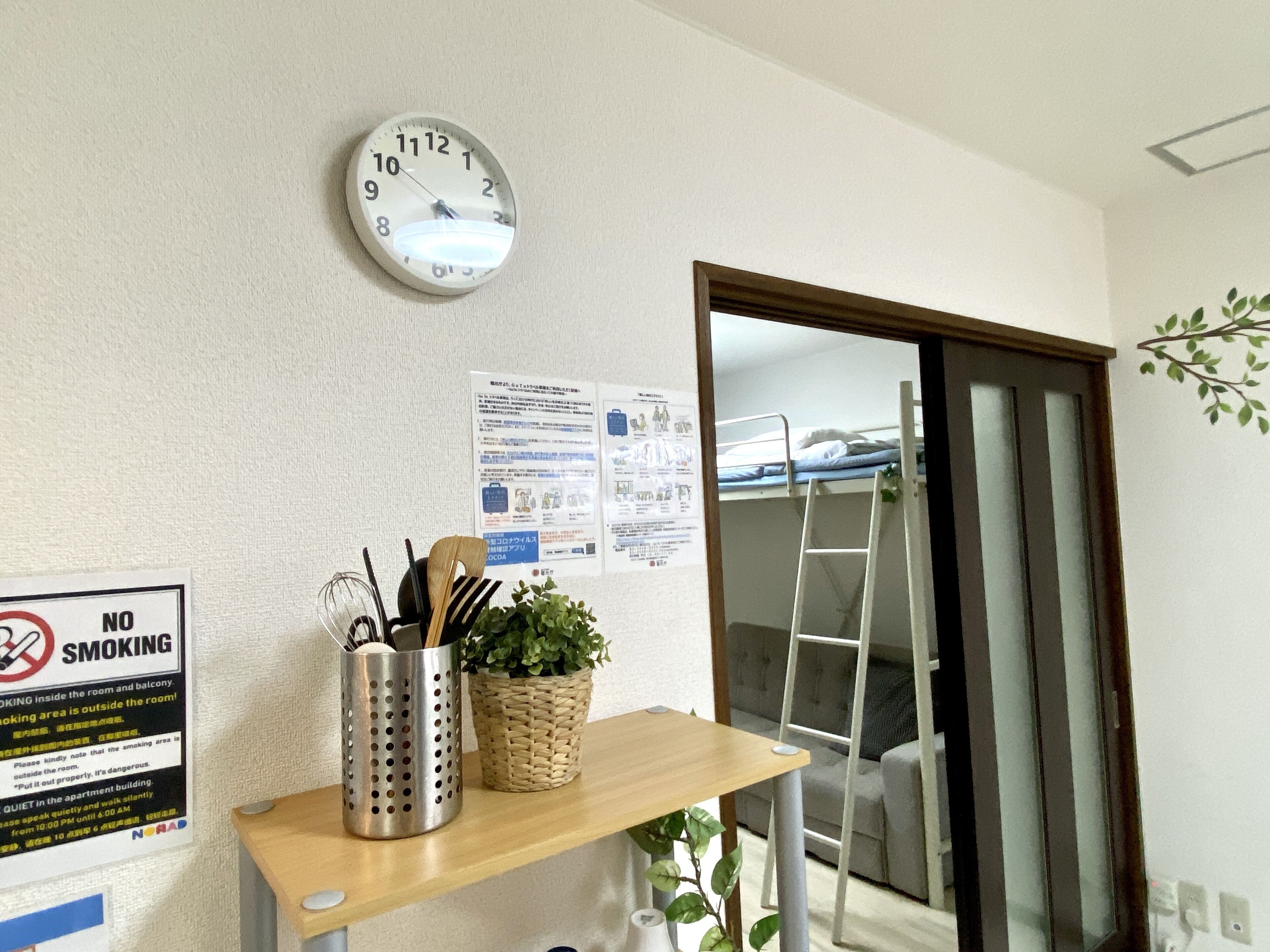 A room with a clock, a 'No Smoking' sign, a wooden shelf with a plant, and a ladder leading to a bunk bed.