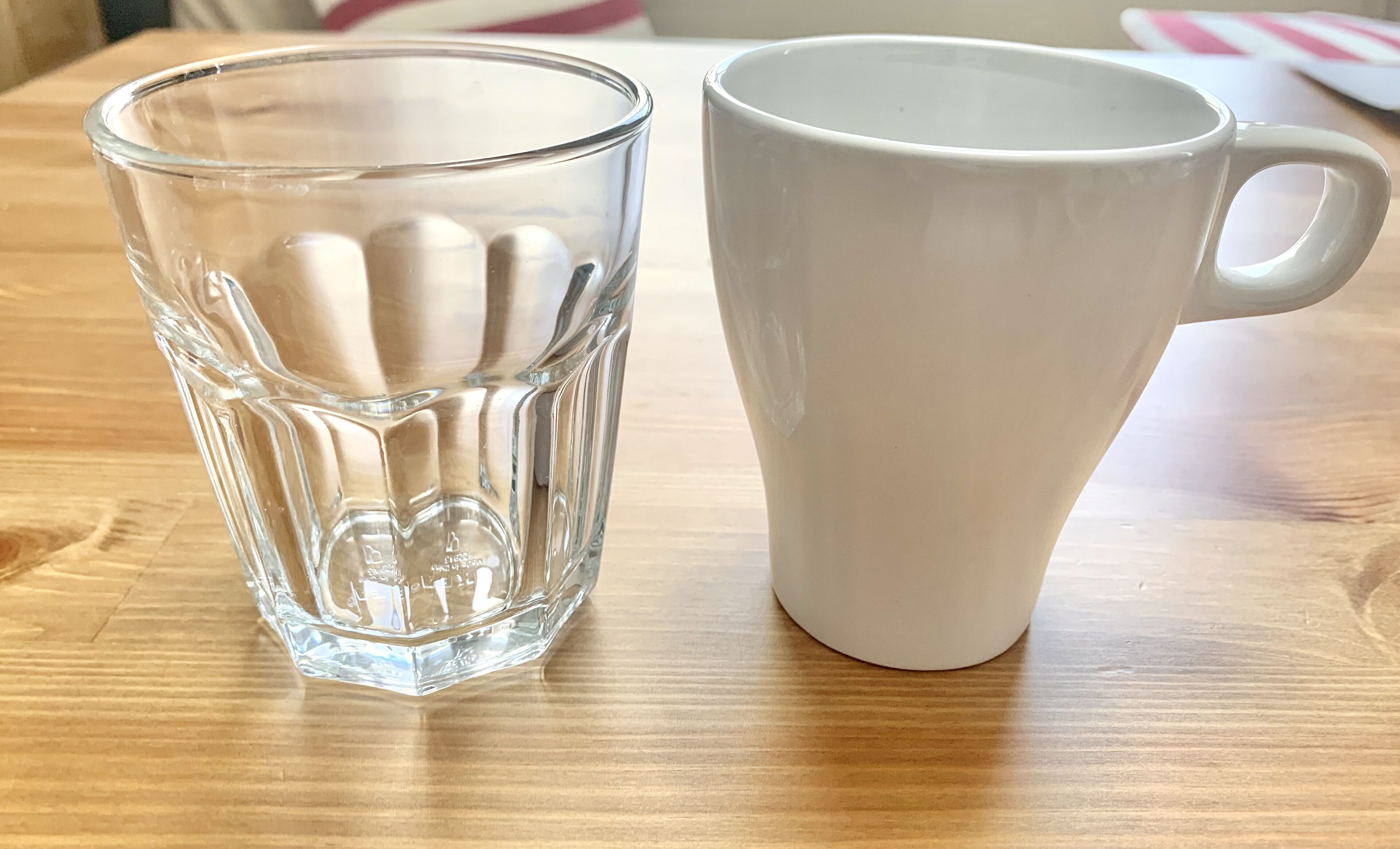 A clear glass and a white ceramic mug on a wooden table.