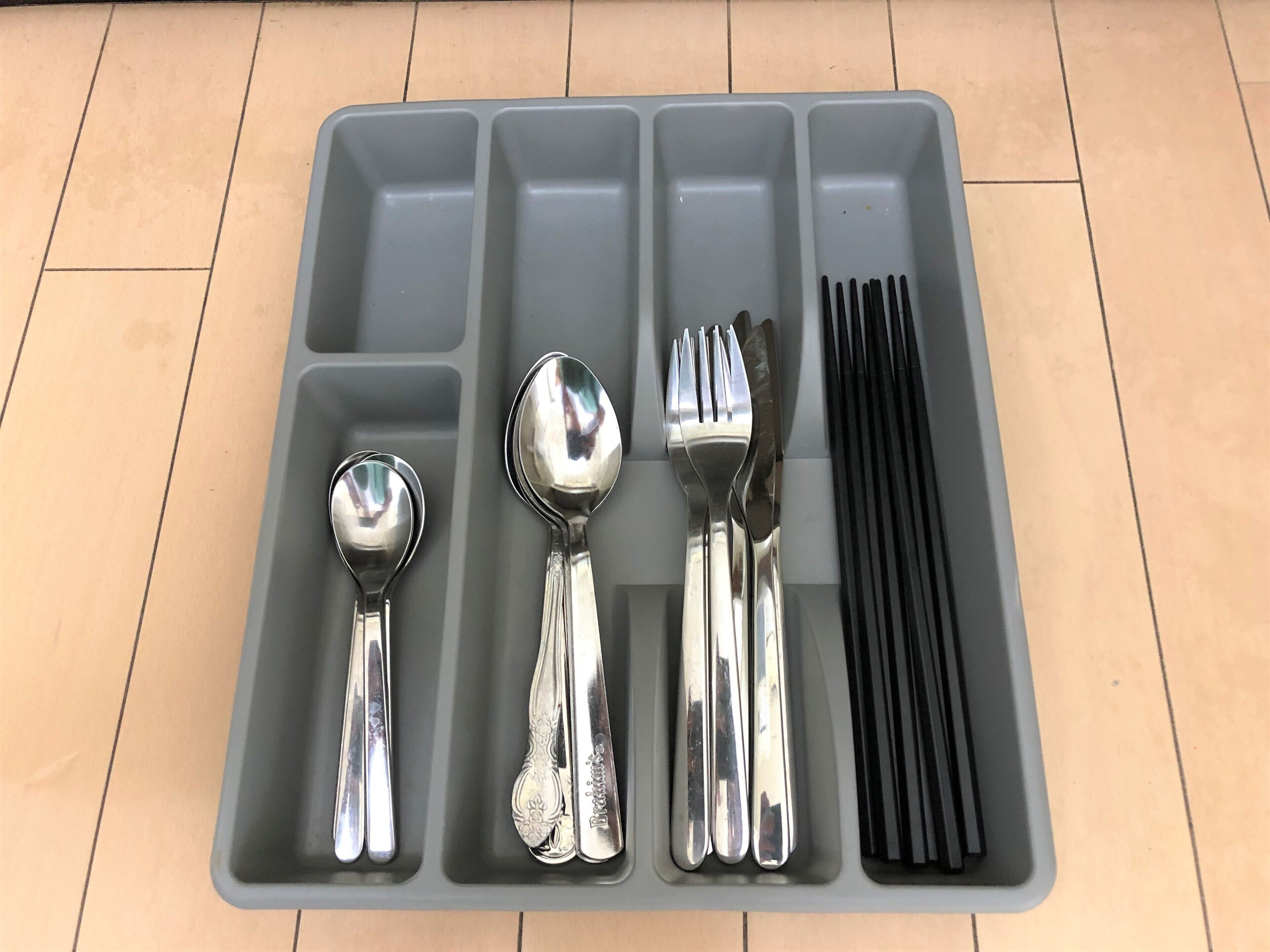 A gray plastic tray with compartments containing various utensils, including spoons, forks, and knives.