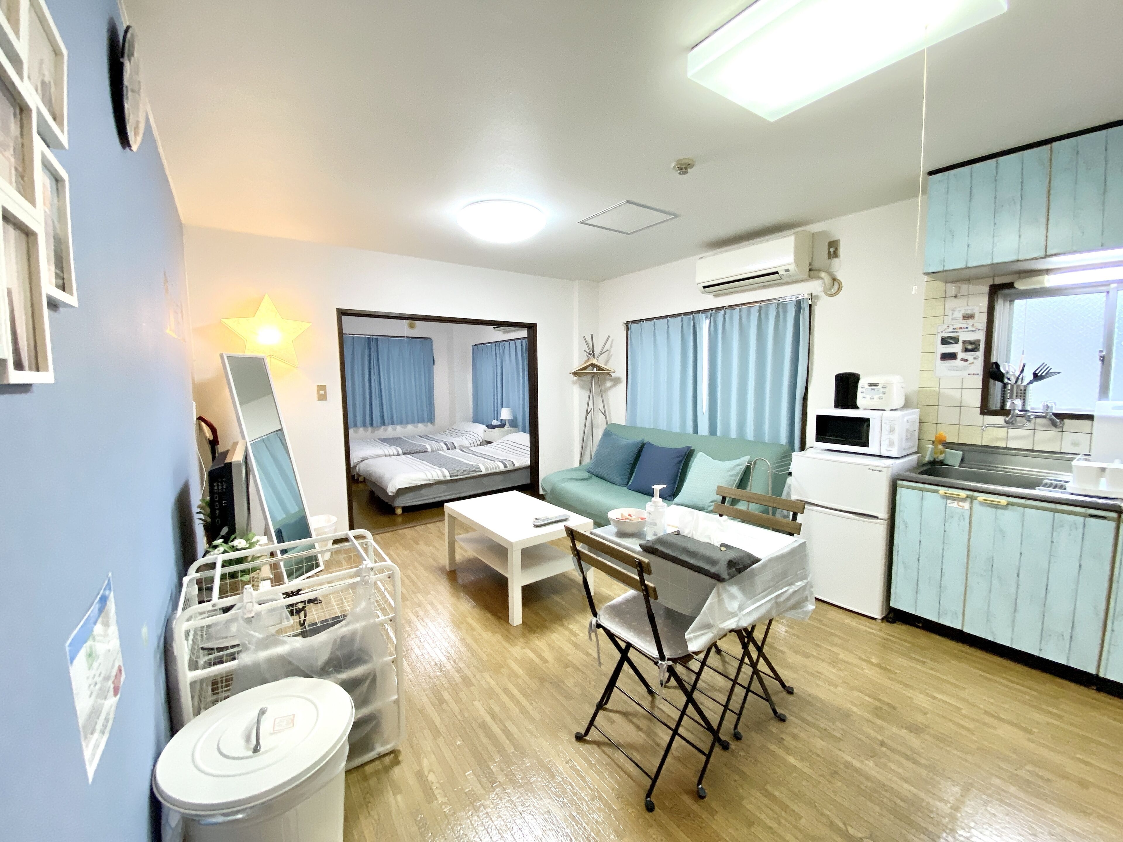 A compact hotel room with a bed, a sofa, a small kitchen area, and a dining table.