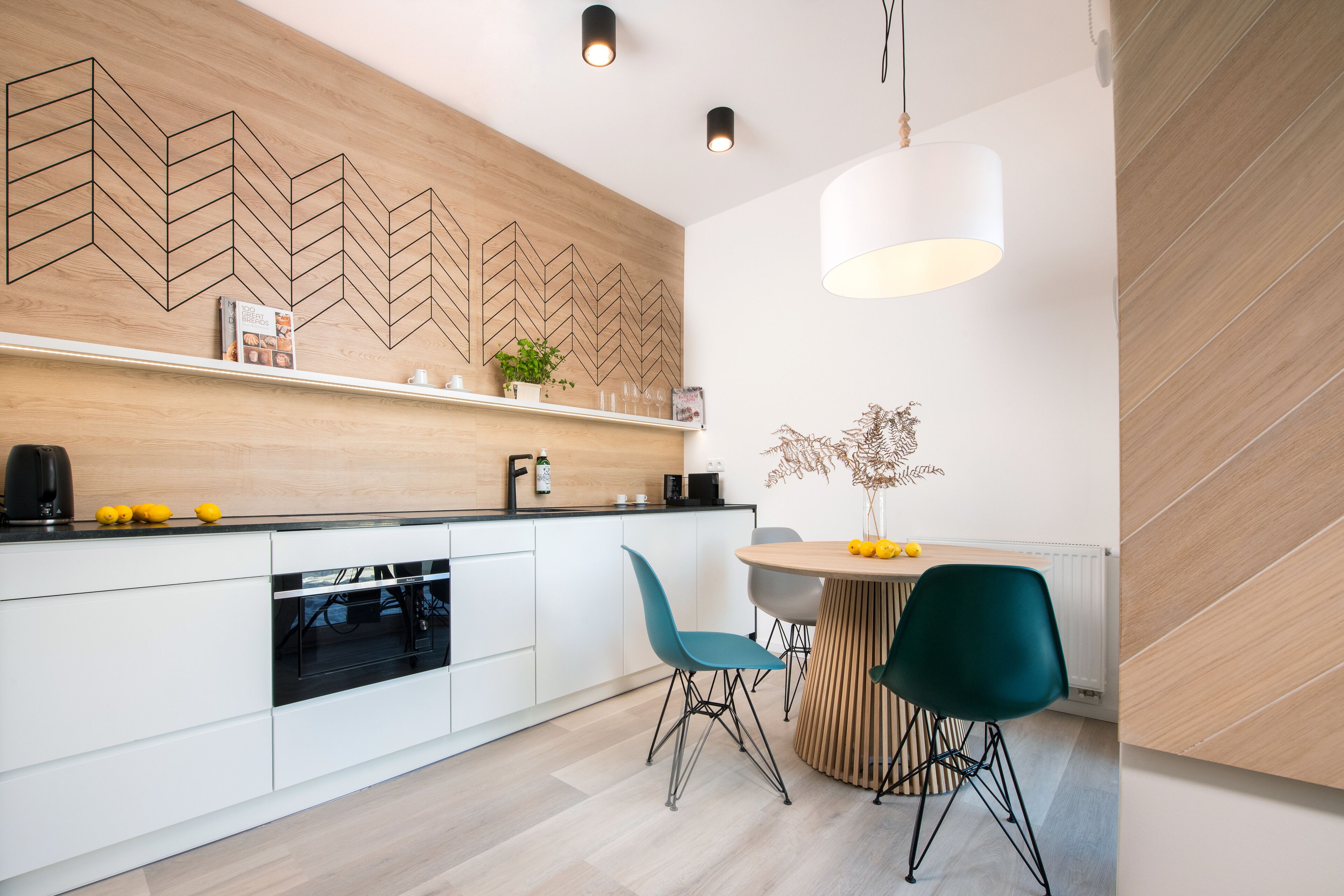 A modern kitchen with white cabinets, a wooden backsplash, and a dining area with teal chairs.