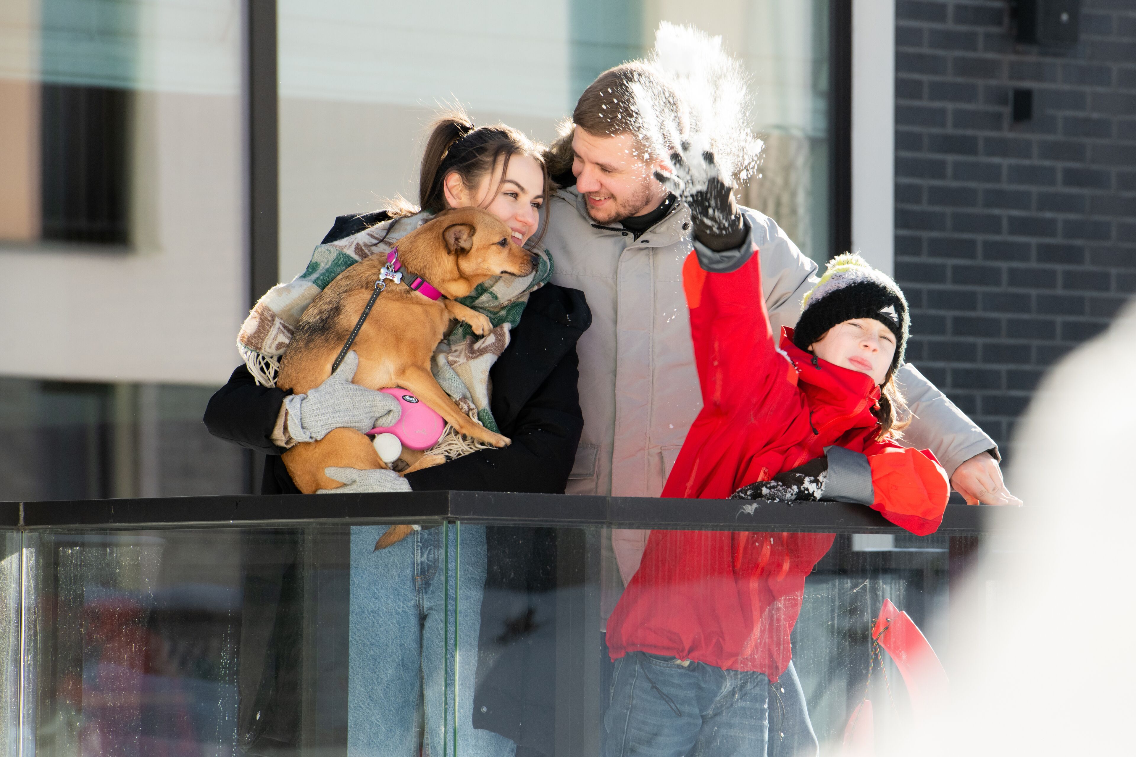 A family with a dog on a balcony with a glass railing.