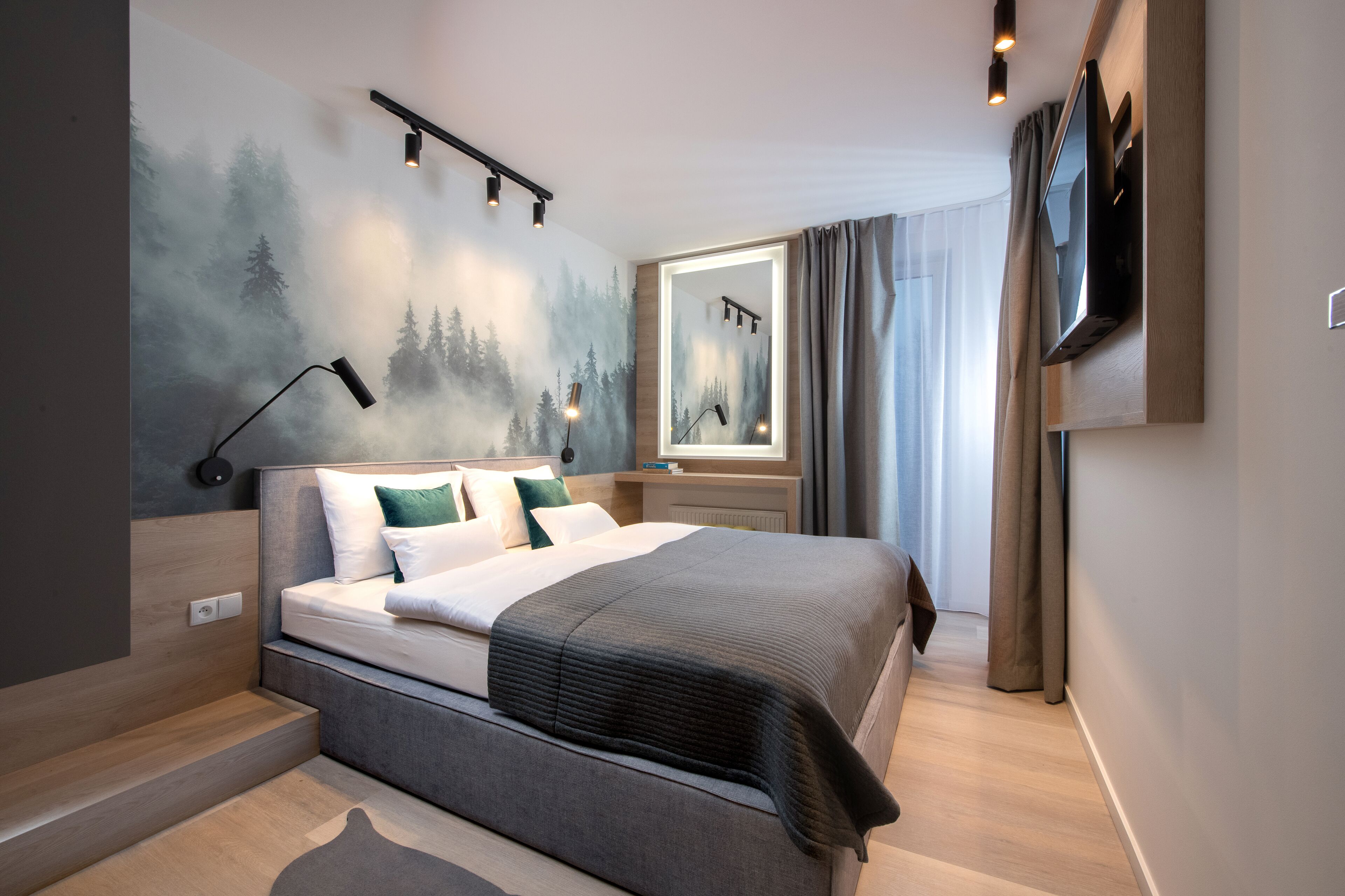 Una camera d'albergo moderna con un grande letto, una TV a parete e un murale raffigurante una foresta.