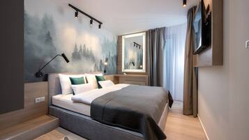 A modern hotel room with a large bed, a mounted TV, and a wall mural of a forest scene.