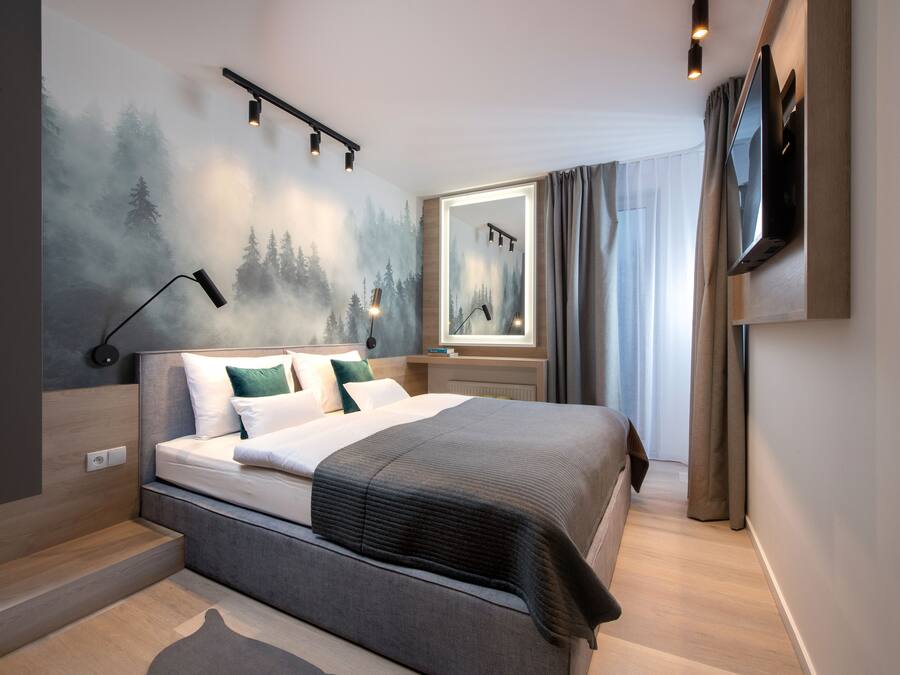 A modern hotel room with a large bed, a mounted TV, and a wall mural of a forest scene.
