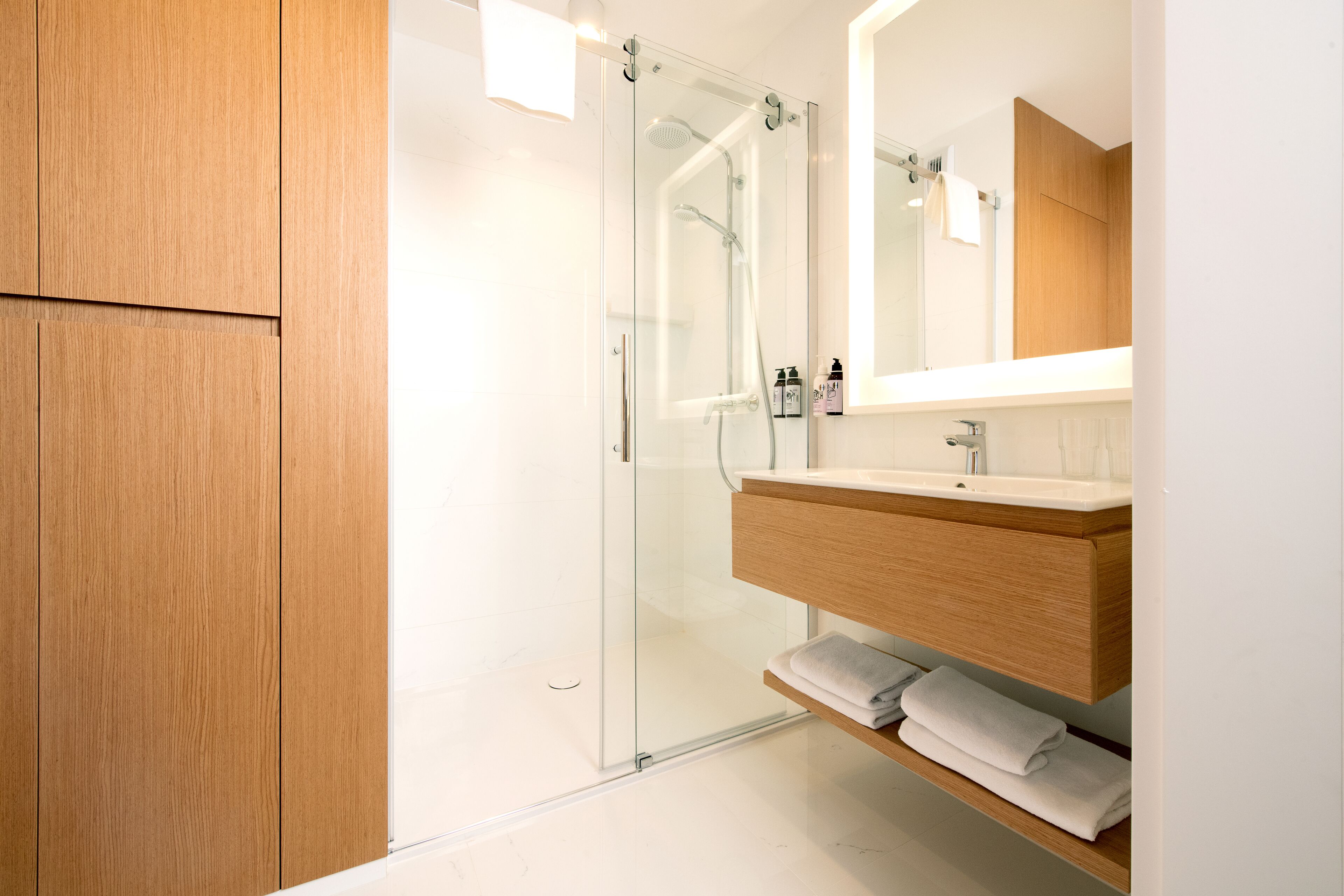 A modern bathroom with a glass shower enclosure, wooden vanity, and a large mirror.