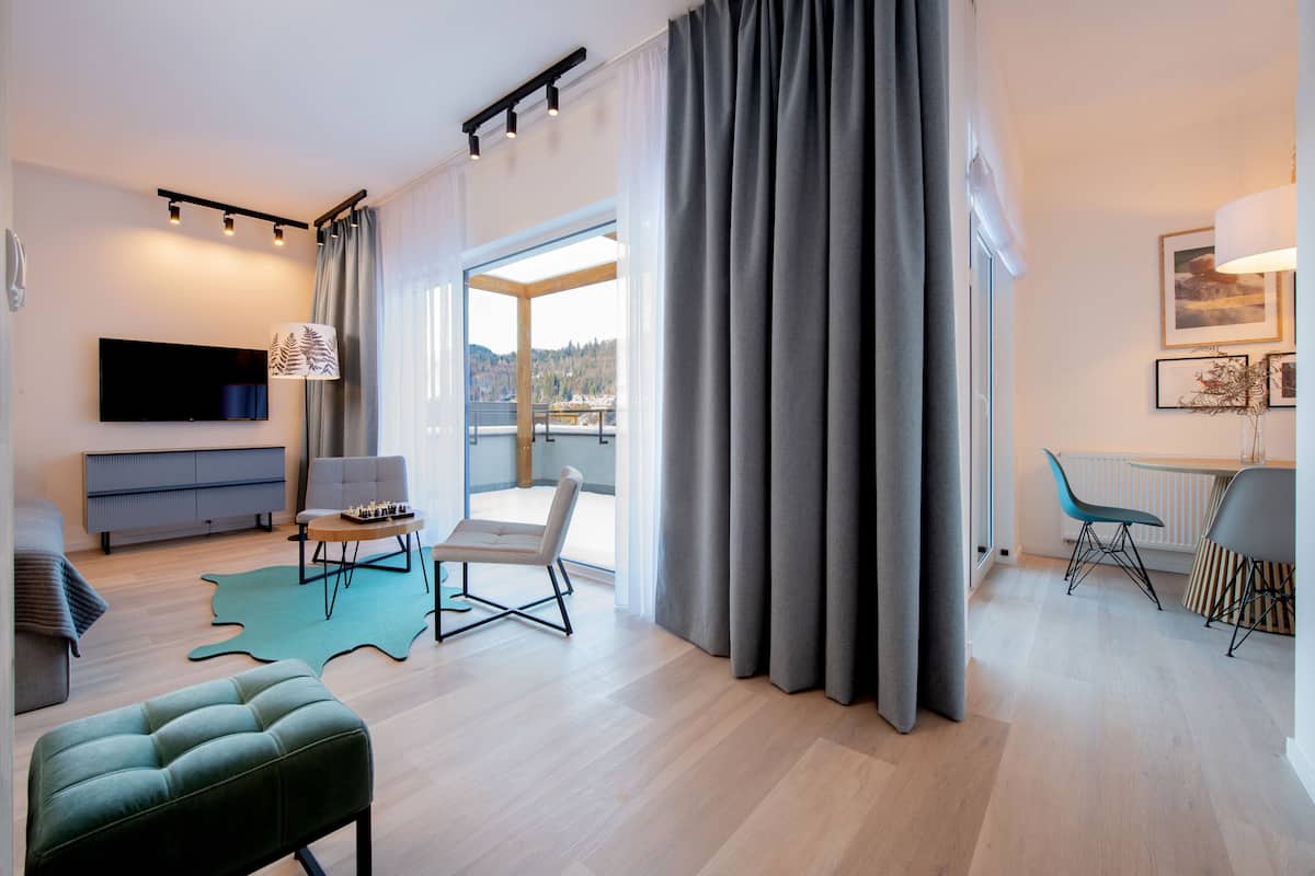 Un salón moderno con televisor de pantalla plana, un sofá, una mesa de comedor con sillas y vistas al exterior.