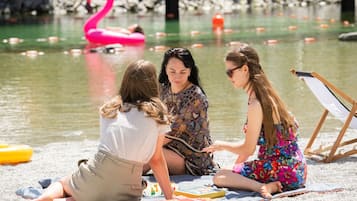 Drie personen zitten op het strand, met een waterlichaam en een roze flamingo opblaasfiguur op de achtergrond.