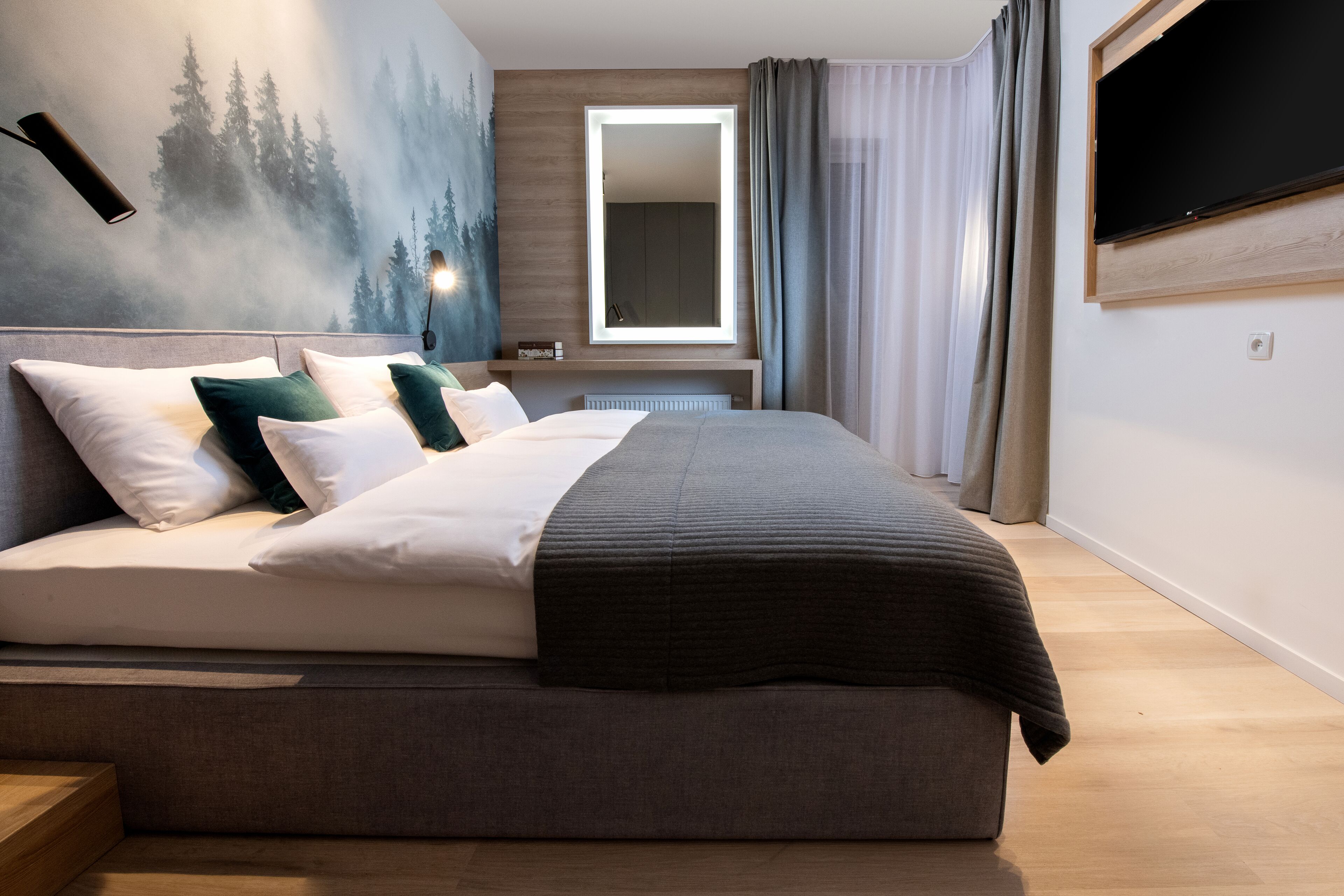 A modern bedroom with a large bed, a bedside table, a mirror, and a TV mounted on the wall.