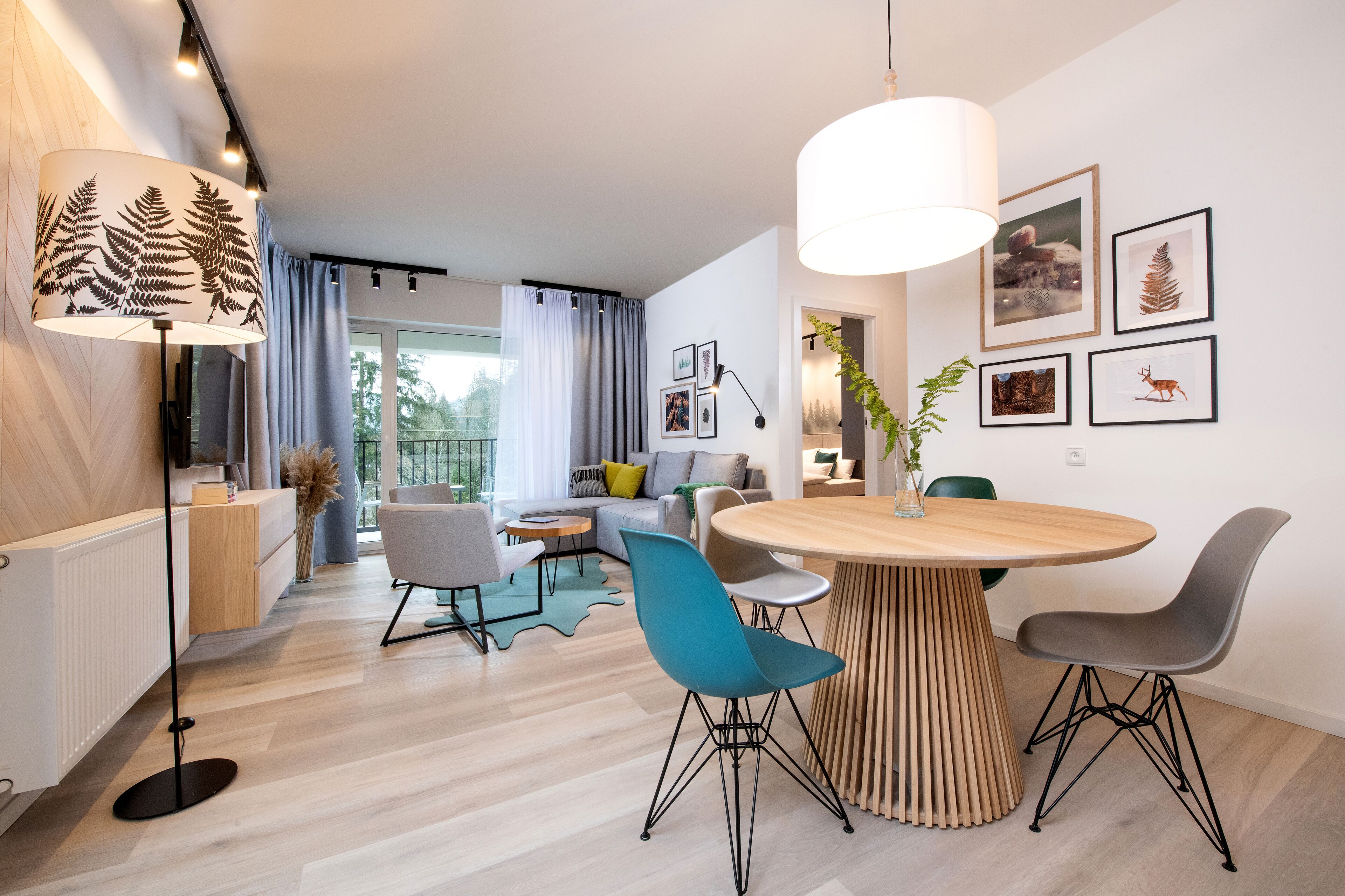 Uma sala de estar moderna com uma mesa redonda de madeira, duas cadeiras, um abajur e um sofá.