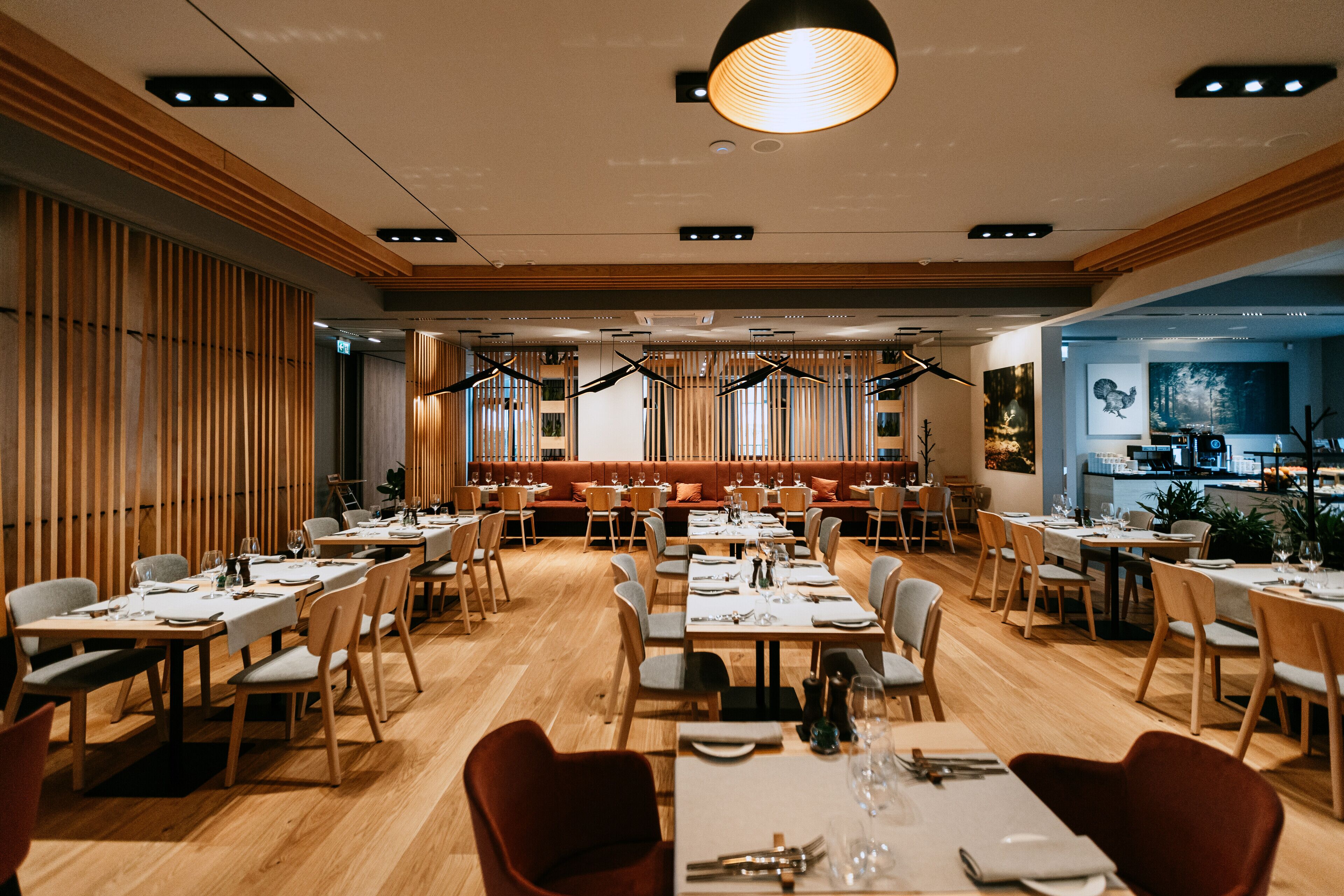 Ein Restaurant mit Holzboden, mehreren Esstischen und einer zentralen Sitzgruppe mit einer niedrigen Bank.