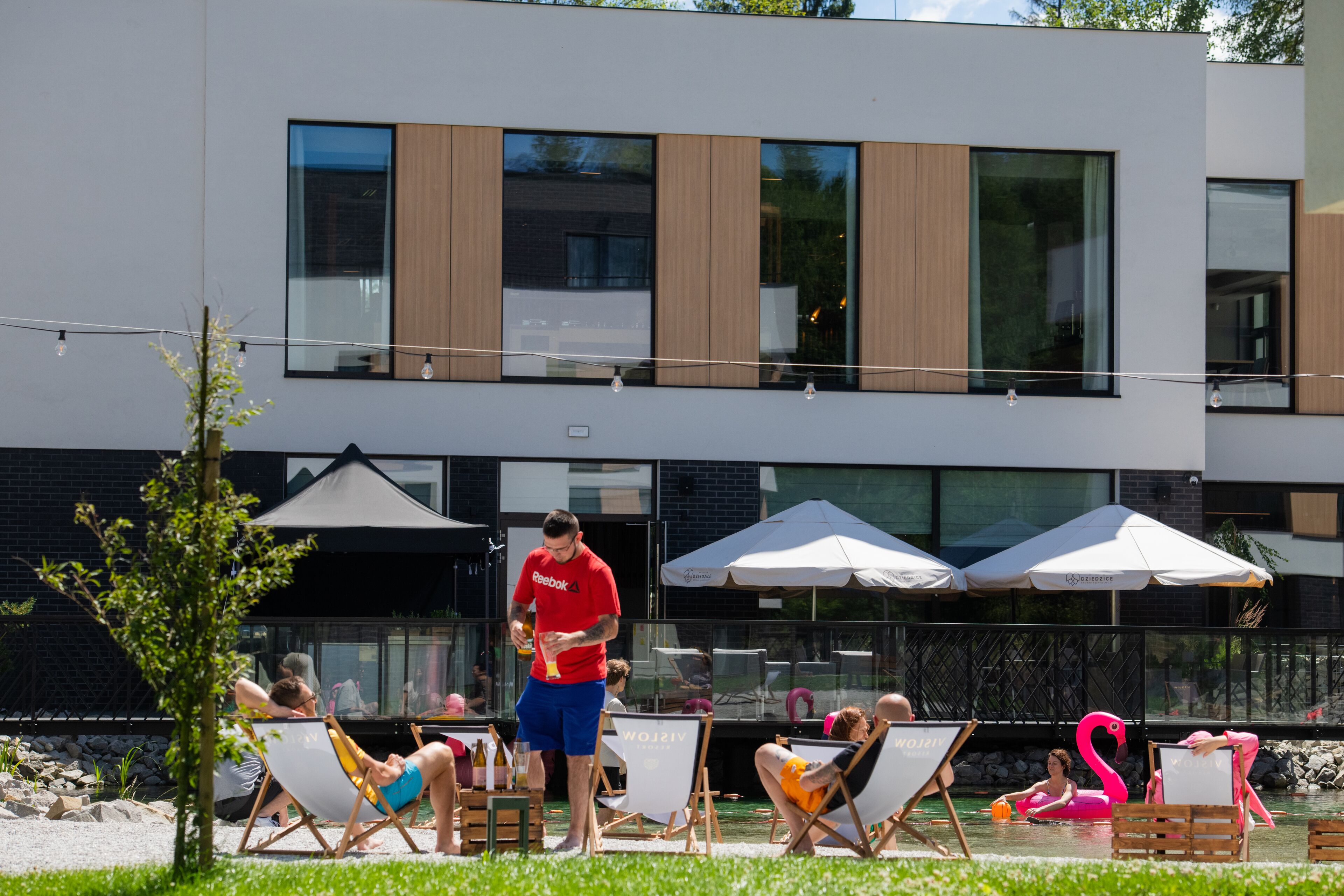 An outdoor pool area with lounge chairs, umbrellas, and a modern building in the background.