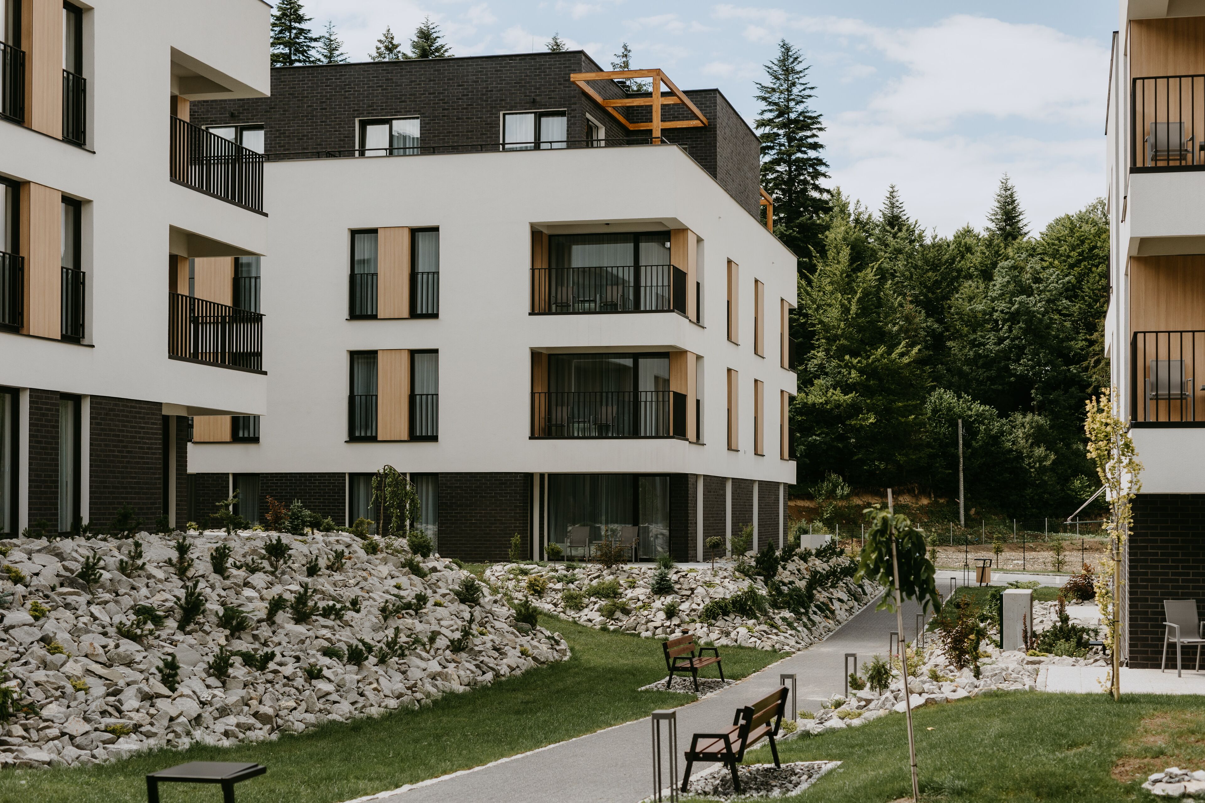 Ein modernes, mehrgeschossiges Wohngebäude mit Balkonen, einem gepflasterten Weg und einem angelegten Garten mit Steinen und Pflanzen.