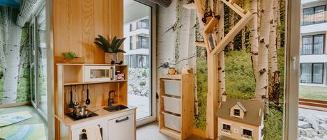 A cozy kitchen with wooden cabinets, a microwave, and a sink. There is a window with a view of a building and greenery outside.