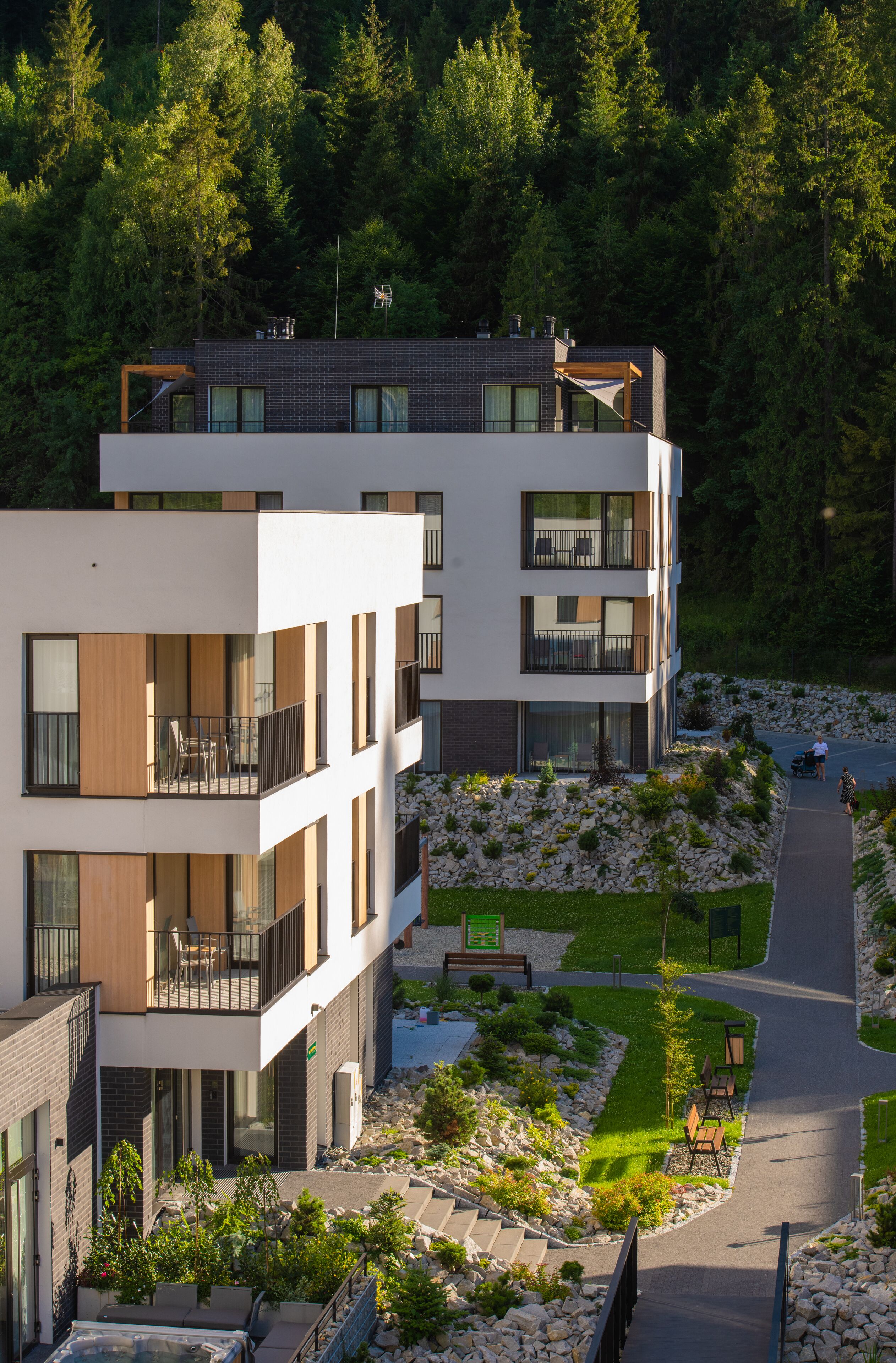 Un immeuble moderne à plusieurs étages, doté de balcons, d’une allée pavée et d’un jardin aménagé.